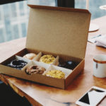 6 beignets dans une boîte avec une tasse et un téléphone portable sur une table